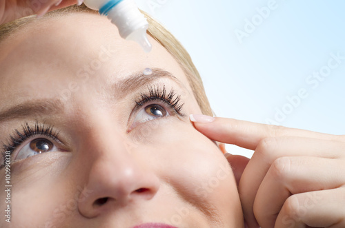 Closeup of young woman applying eye drops, selective focus only on right eye. Drop captured in mid air/ eye drops with vitamins/ eye care