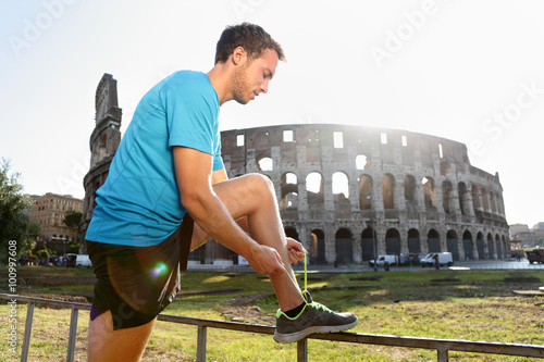 Canvas Print Young male jogger running tying shoelace against Colosseum