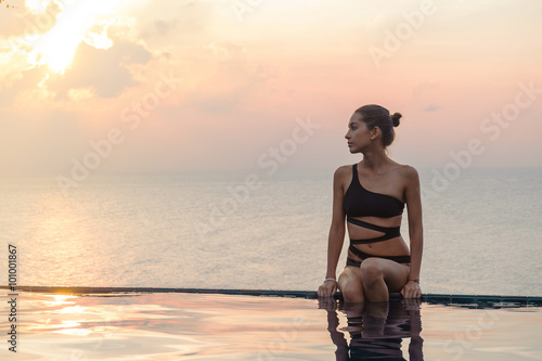 Obraz na płótnie Woman is sitting at the swimming pool on sunset w salonie