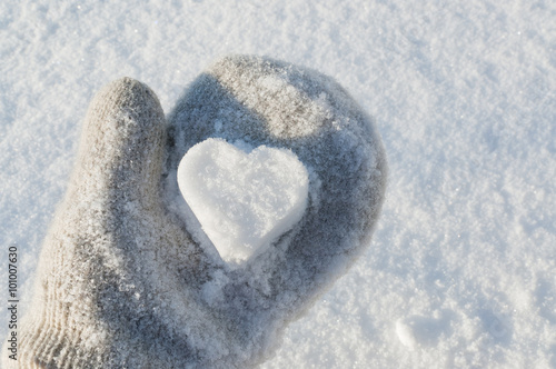 Holding white snow heart in hand with snowy woollen mitten.