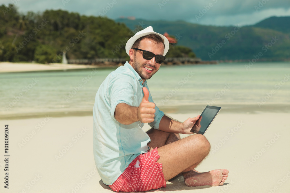man giving thumbs up while sitting on the beach with ipad