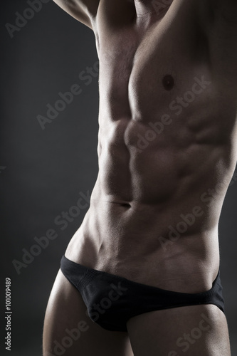 Handsome muscular bodybuilder posing on gray background. Low key close up studio shot