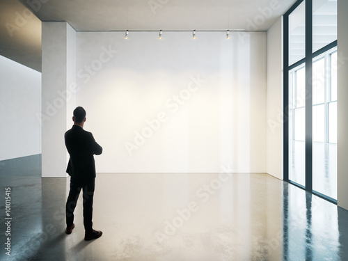 Businessman stands in blank white museum interior with concrete floor. Horizontal