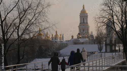 Family Parents And Kids Are Walking Wintery Park by a Bridge Two Young Girls are Standing on a Bridge and Going to Take a Photo Kiev Towers Cathedral