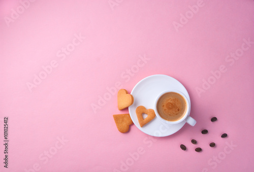 Cup of coffee on bright pink grainy paper surface with heart shaped cookies and a few coffee beans on the side