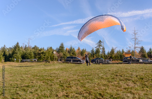 Paraglider is ready to take off over a green hill