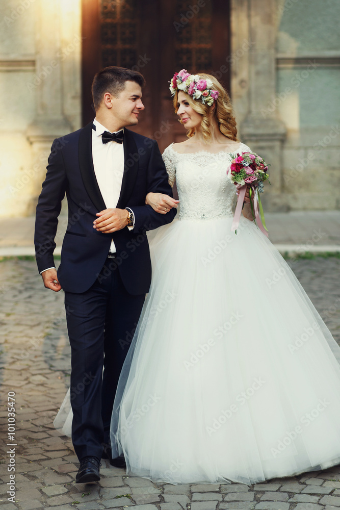 Confident elegant groom and beautiful shy bride holding hands ou