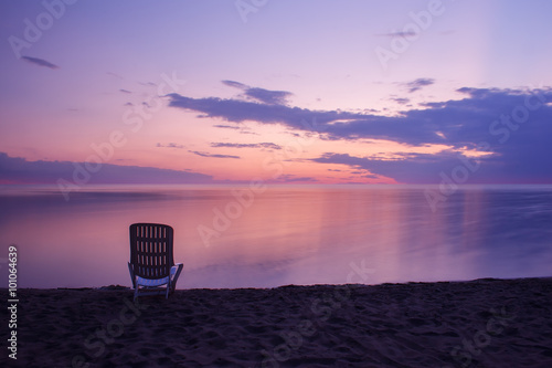 one chair standing on the beach at sunset