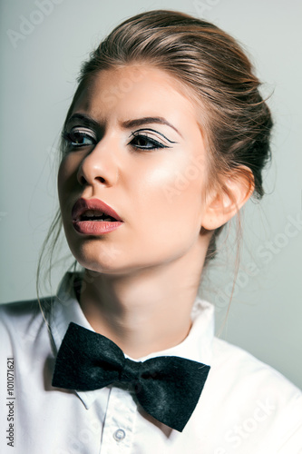 Obraz na plátně Beautiful young woman wearing a shirt and bow tie against a gray background
