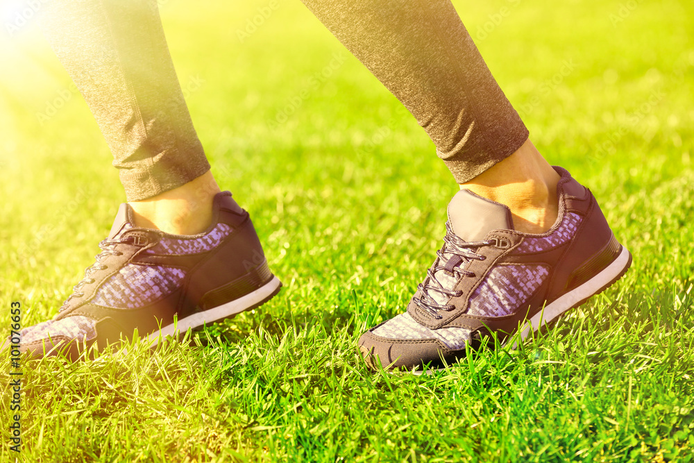 Sports woman legs in sneakers on grass outdoor