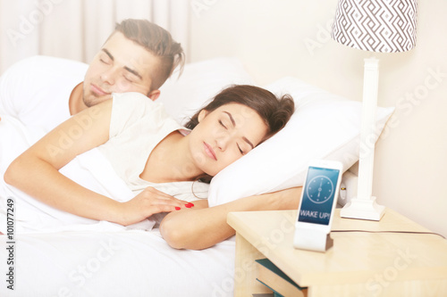 Young couple waking up with mobile alarm clock