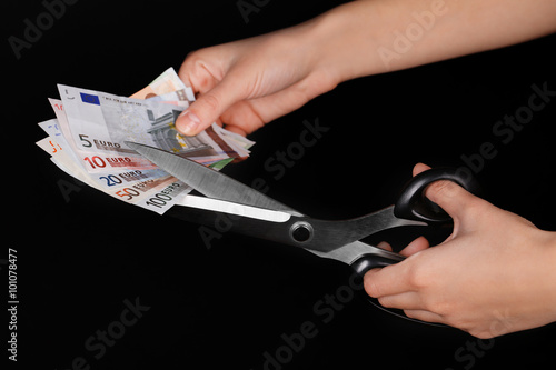 Hands with scissors cutting Euro banknotes, on black background © Africa Studio