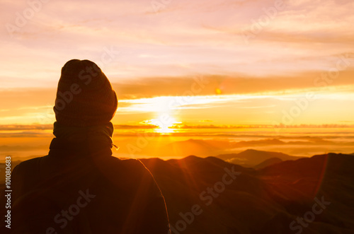 Man standing on a ledge of a mountain, enjoying the beautiful sunset.