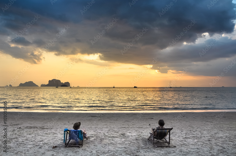 Two girls in beach chairs admiring the sunset at sea.