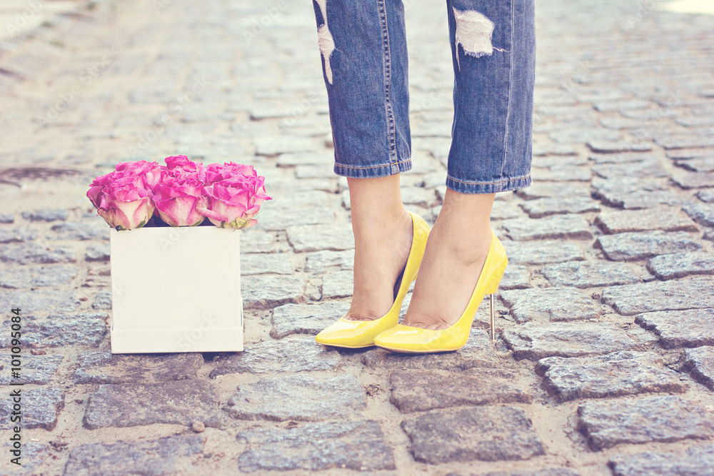 The bouquet of pink roses and female legs in jeans and yellow shoes with heels.