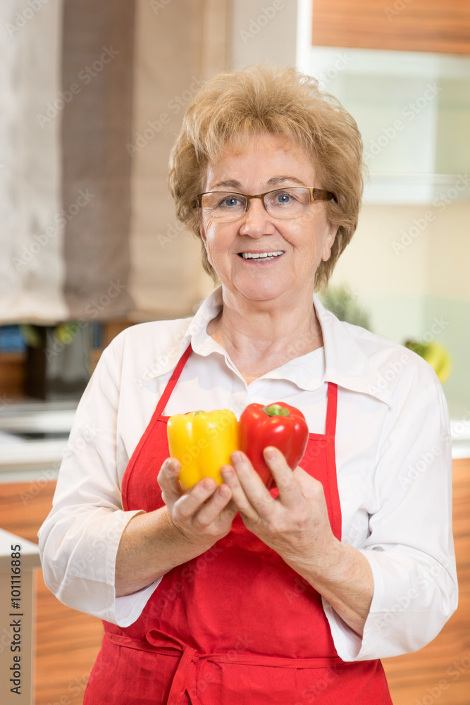 Kochende Seniorin mit zwei Paprika