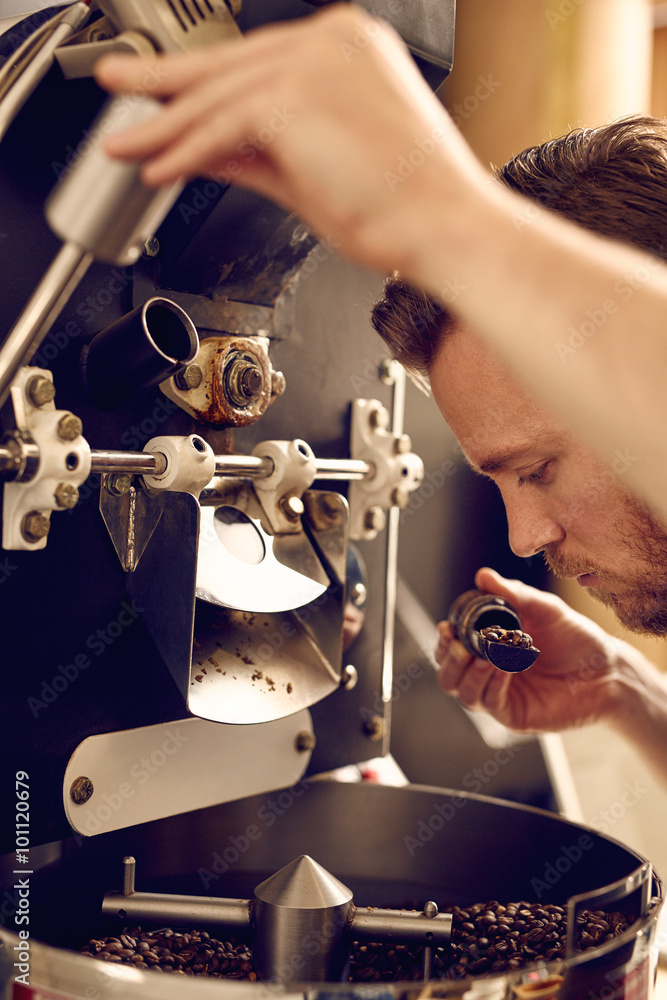 Man operating a modern coffee roasting machine and smelling the 