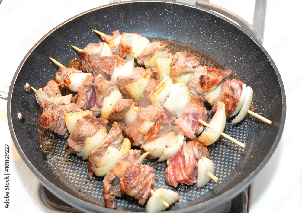 four shashlik skewers roasting in a frying pan four shashlik skewers roasting in a frying pan
