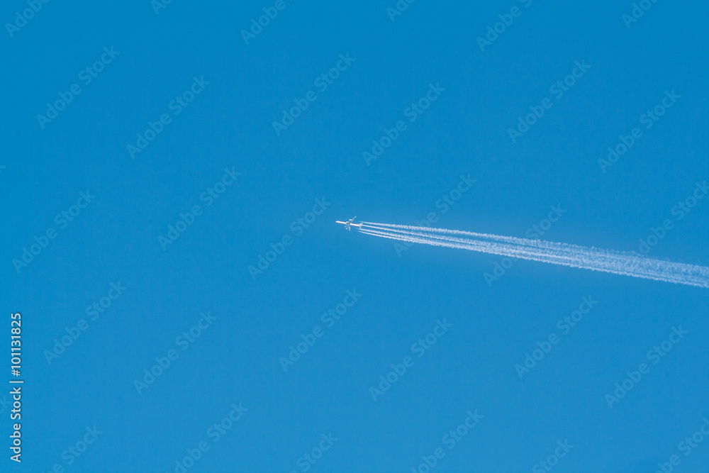 White airliner with a vapor trail in a clear blue sky
