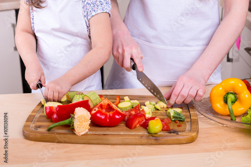 mother teaching daughter to cut vegetables