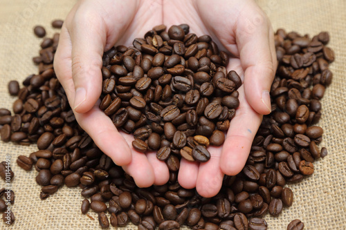 roasted coffee beans pouring out of cupped hands into a burlap s