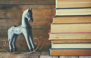 stack of old books next to decorative rocking horse wooden table. vintage filtered image
