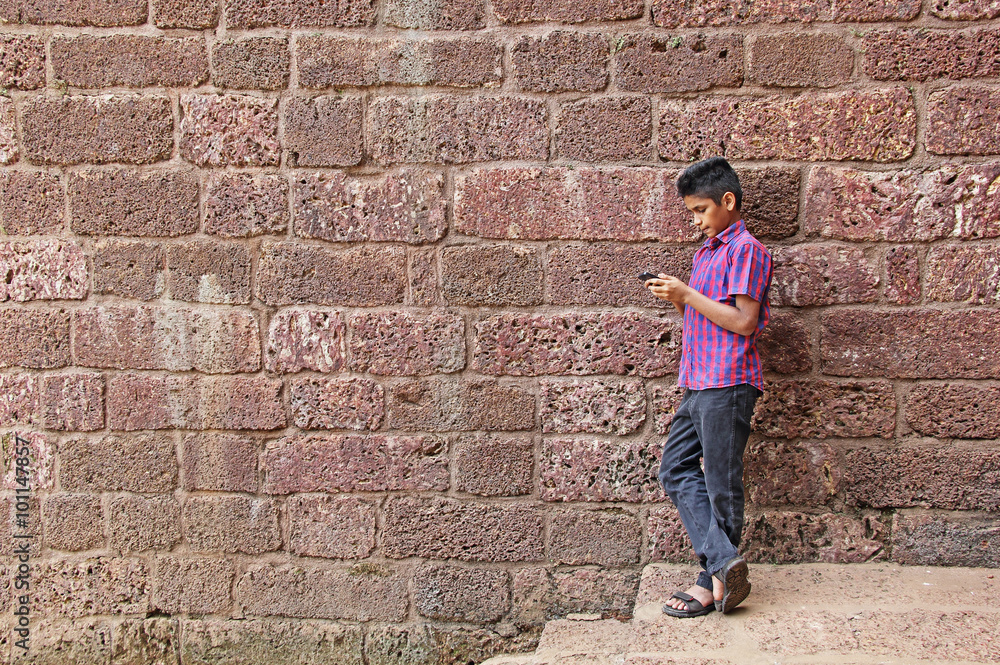 Smart young man working seriously on smartphone, leaning against red brick wall