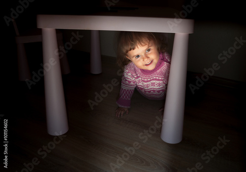 The little girl looks out from under the table.