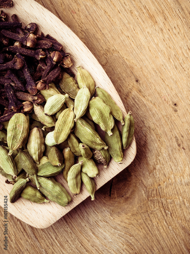 cardamom pods and cloves on wooden spoon cardamom pods and cloves on wooden spoon