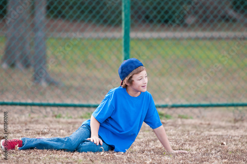 Young boy with baseball hat sitting in grass