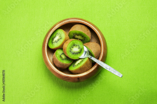 Juicy ripe kiwi fruit in wooden bowl on green napkin with spoon