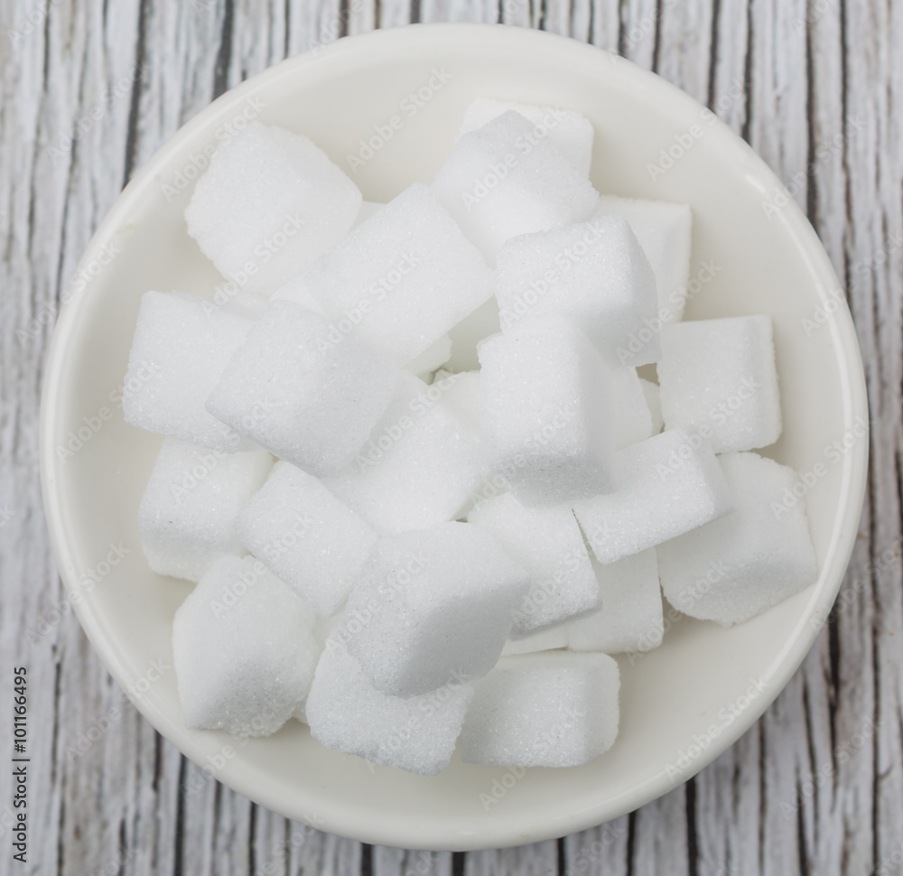White sugar cube in white bowl over wooden background