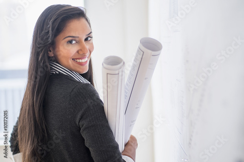 Hispanic architect carrying blueprints in office