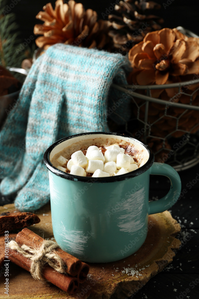 Mug of hot cacao with marshmallow and gloves on black table