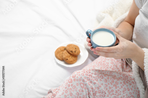 Woman in pajamas holding cup of milk on her bed