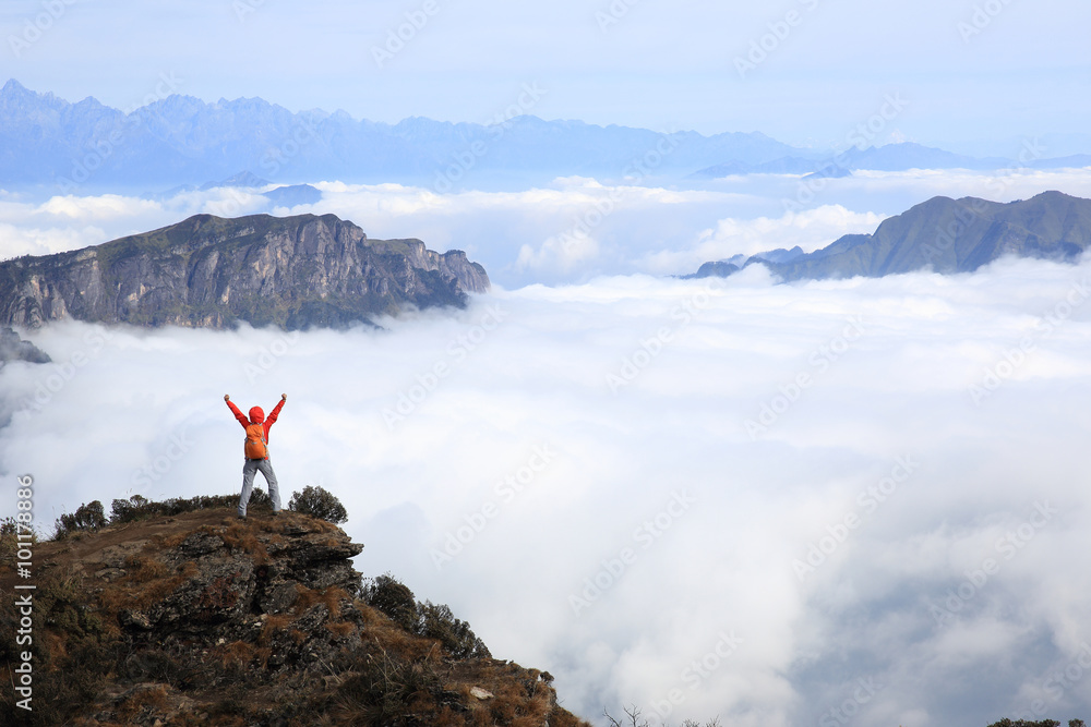 cheering young woman hiker open arms at mountain peak face to the mountain summits