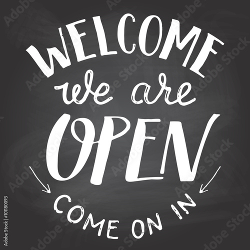 Welcome we are open. A welcome sign for cafes or shop visitors on blackboard background with chalk. Hand lettering