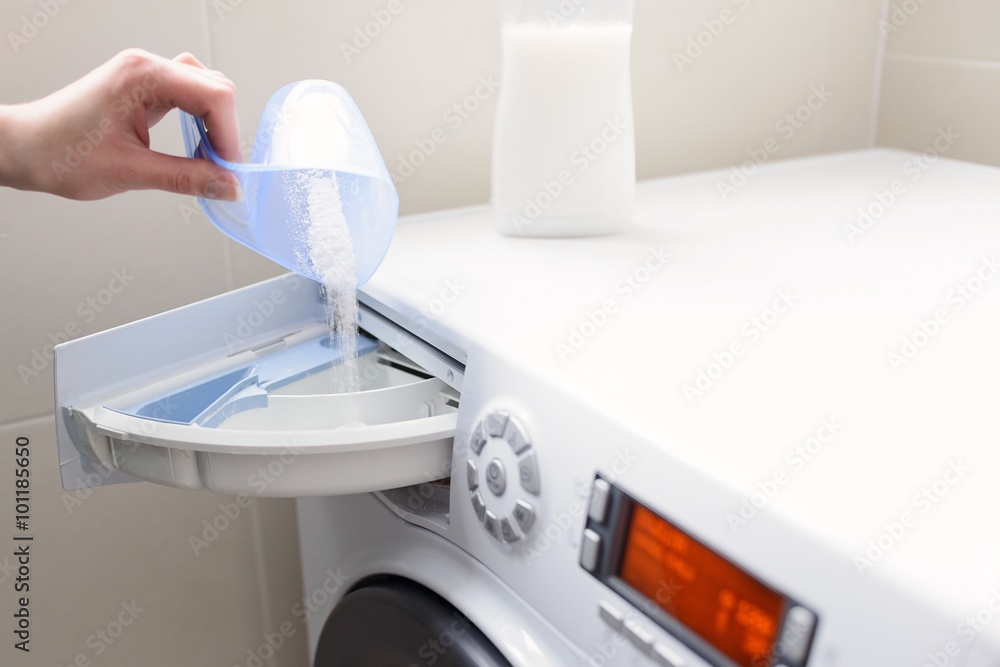 Closeup on woman's hand pouring detergent into the washing machine