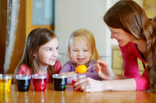 Young mother and her two daughters painting Easter eggs
