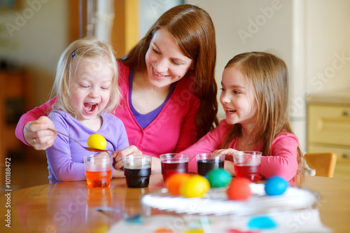 Young mother and her two daughters painting Easter eggs