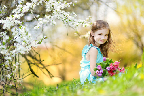 Adorable little girl holding tulips for her mother in cherry garden © MNStudio