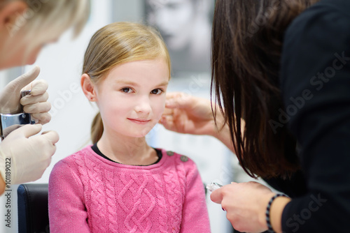 Adorable little girl having ear piercing process in beauty center