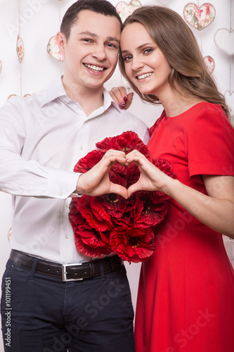 Beautiful young couple in love with a bouquet flowers showing the form of heart hands. Valentine's Day. 