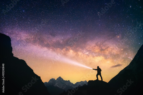 Silhouette of the man standing against the Milky Way in the mountains with a flashlight in his hands. Nepal, Everest region, view of the mount Thamserku (6,608 m) from Thame village (3,750 m). photo