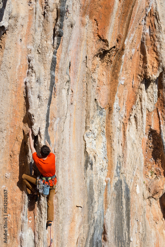 Young man climbing on a limestone wall with wide valley on the background Young man climbing on a limestone wall with wide valley on the background
