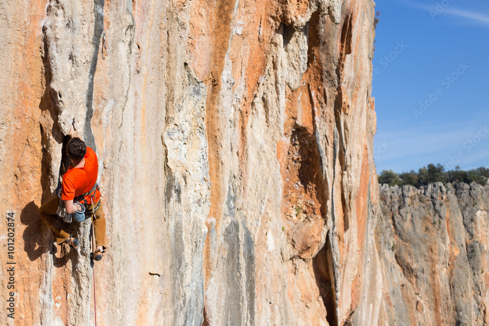 Young man climbing on a limestone wall with wide valley on the background Young man climbing on a limestone wall with wide valley on the background