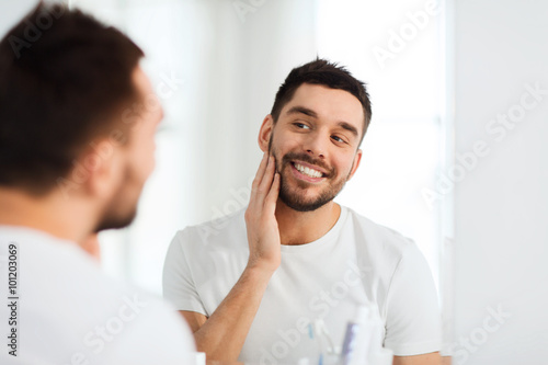 happy young man looking to mirror at home bathroom