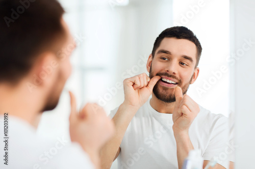 man with dental floss cleaning teeth at bathroom