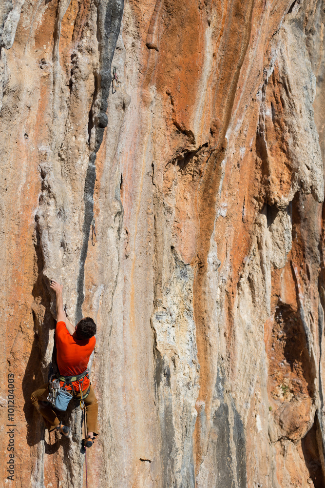 Young man climbing on a limestone wall with wide valley on the background Young man climbing on a limestone wall with wide valley on the background