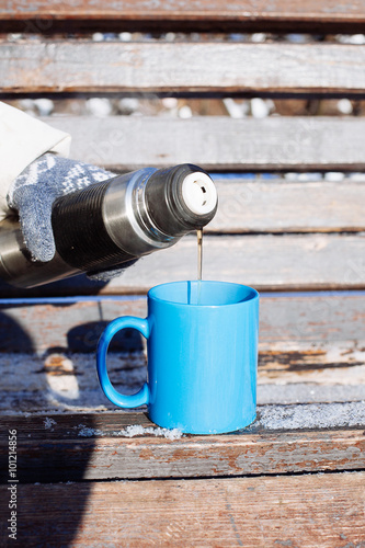 Woman pouring a hot drink in mug from thermos